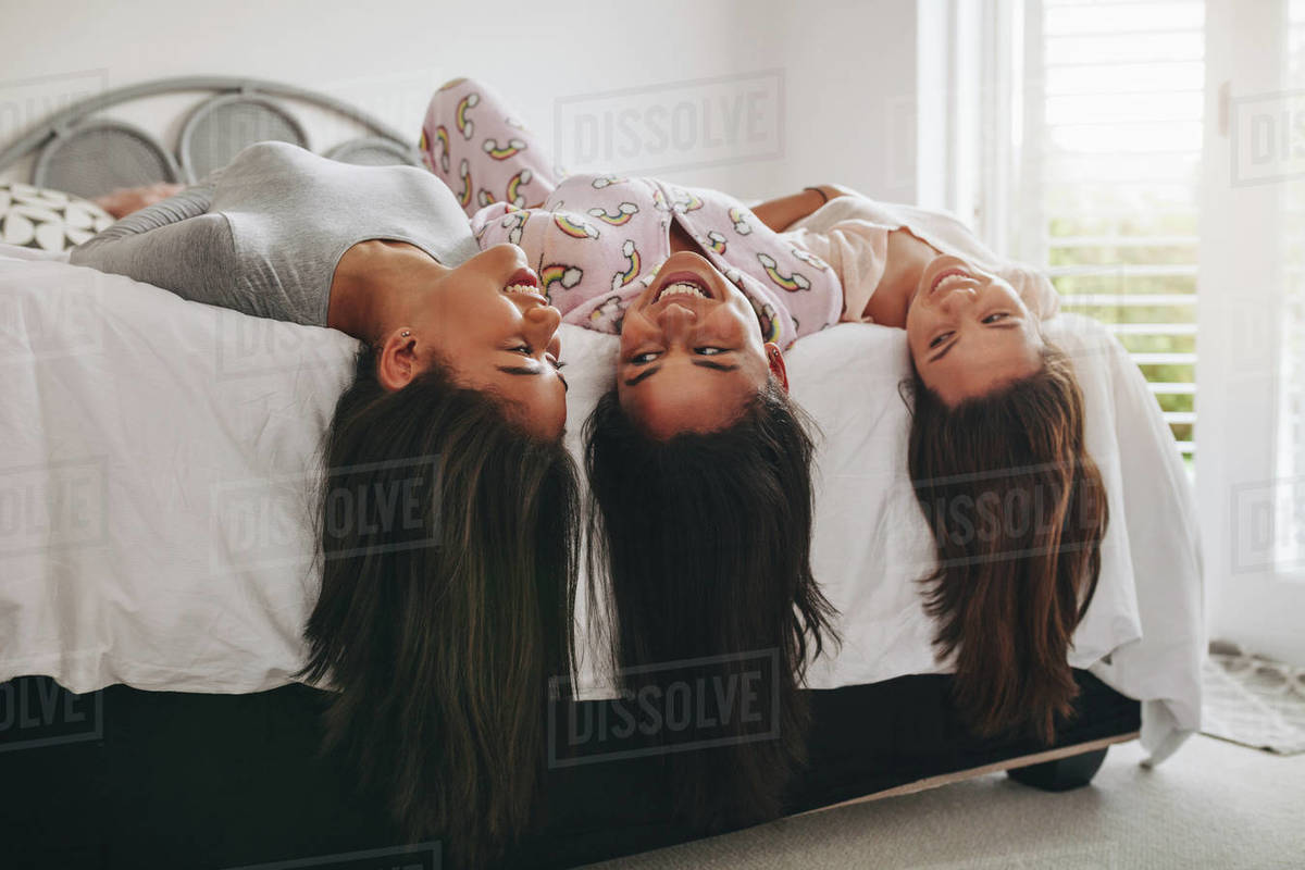 Teenage girls lying on the edge of bed with their hair hanging down