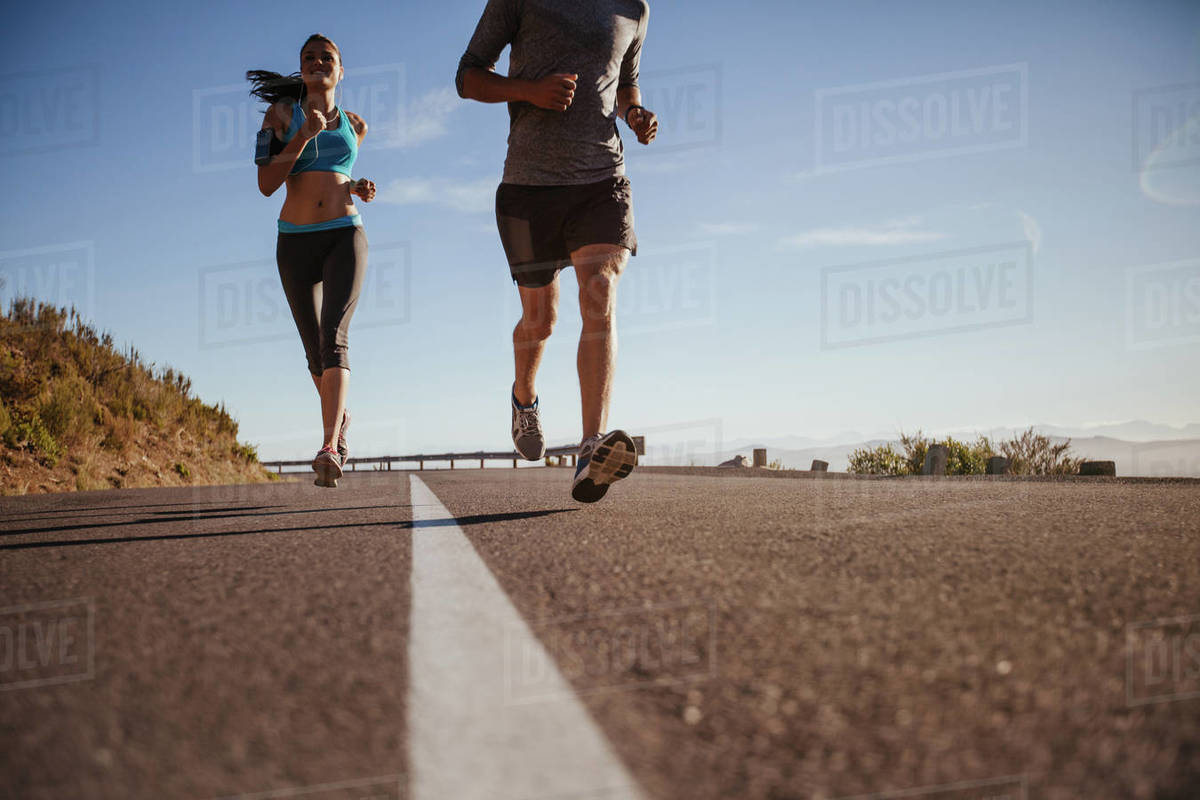 Low angle shot of young woman running on road with man in front on a