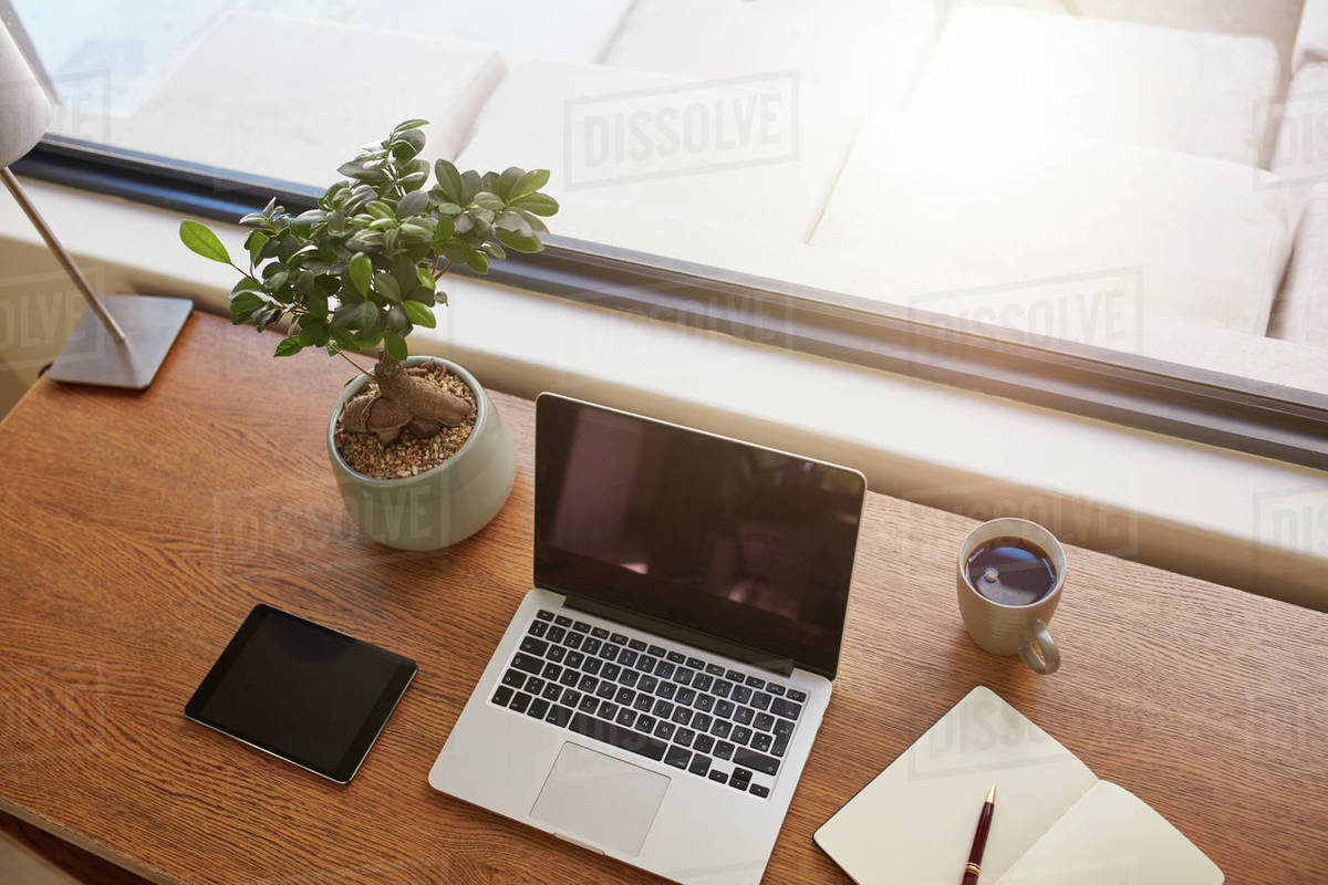 Top view shot of laptop computer, digital tablet, potted plant, diary and a  cup of coffee on wooden table. Modern work desk by a window. - Royalty-free  Stock Photo | Dissolve