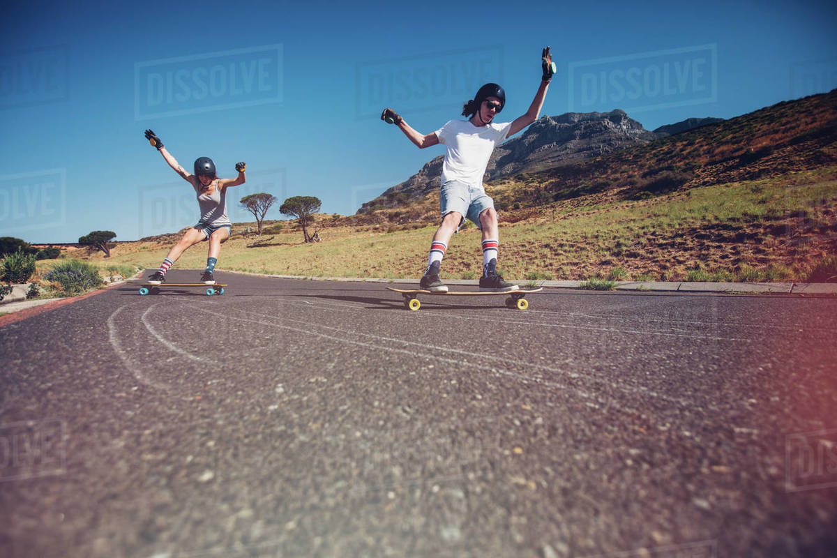 Young man and woman skateboarding on the road. Young couple practicing skating on a open road. Royalty-free stock photo