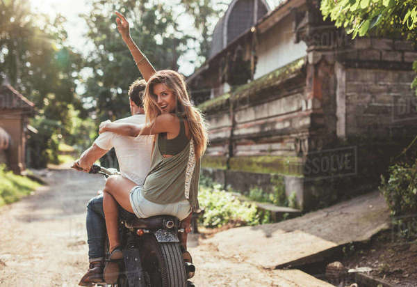 Rear view shot of young couple enjoying motorcycle ride on village road ...