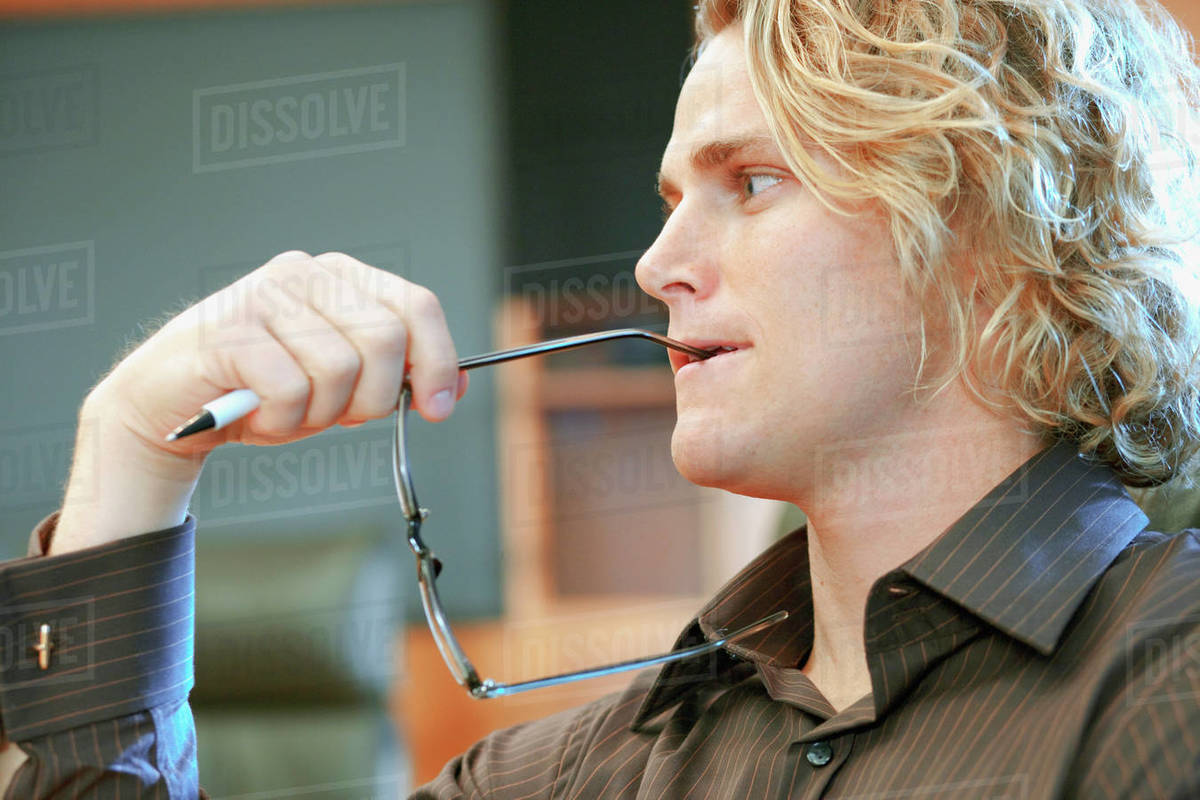 Serious Caucasian businessman biting eyeglasses Stock Photo Dissolve