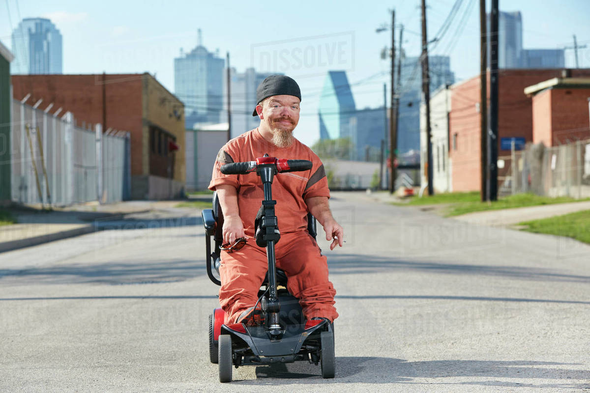 Portrait of male adult little person in the street in Texas on a mobility scooter looking into
