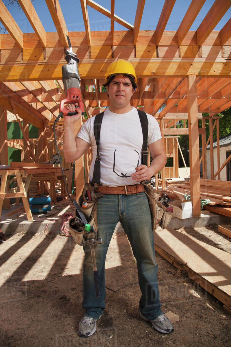 Construction worker wearing a hard hat, tool belt and holding an