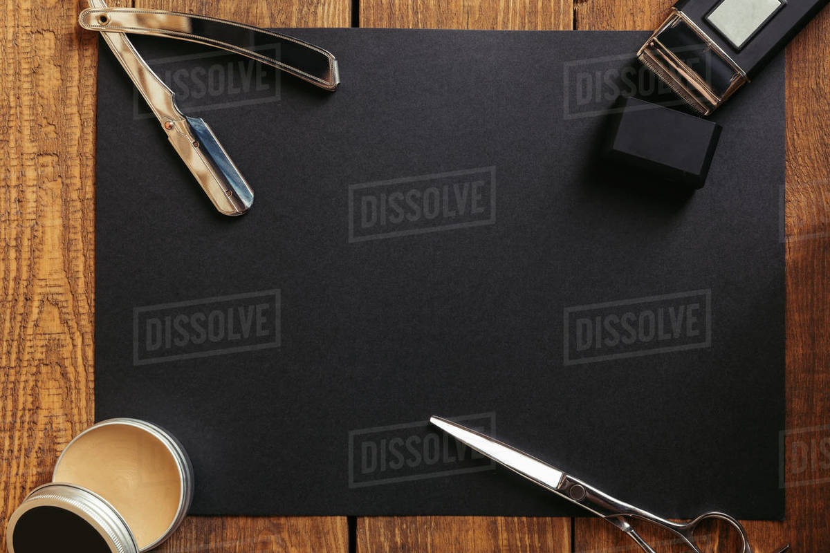 Top view of hair wax, scissors and straight razor on black surface in