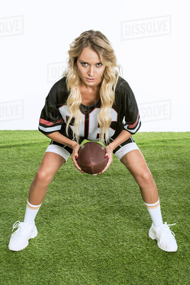 serious young woman in american football uniform holding ball