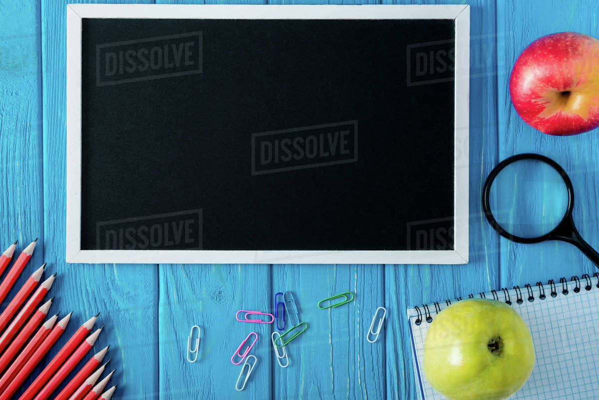 Top view of blank chalkboard and empty textbook, apple, magnifier