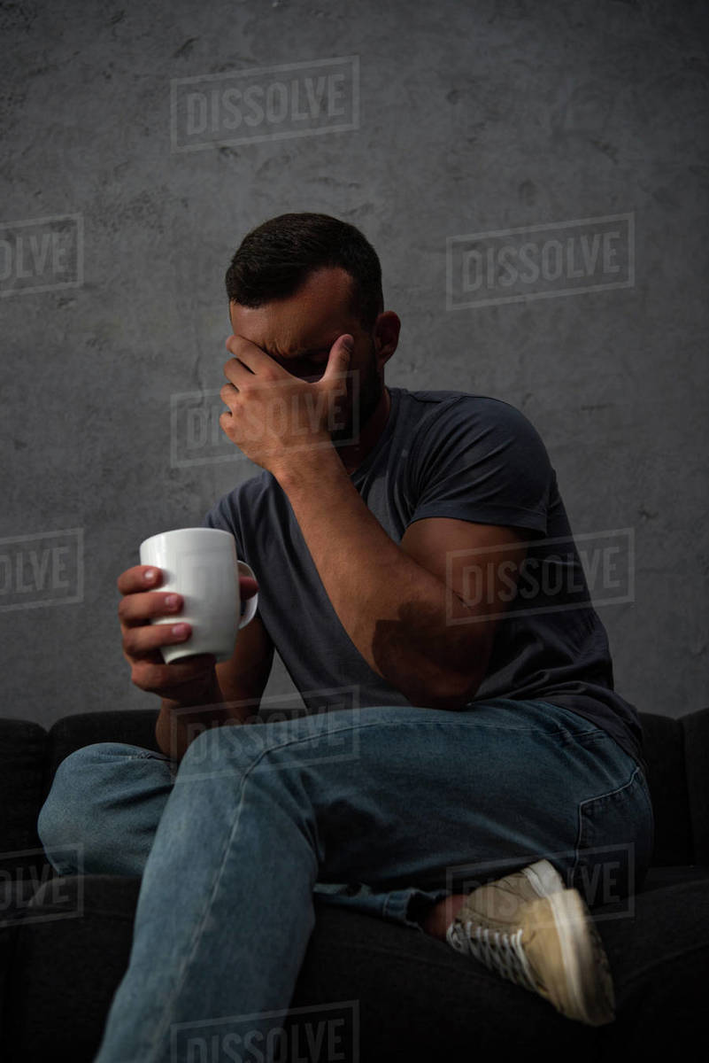 Depressed crying man holding cup of coffee sitting at home Stock