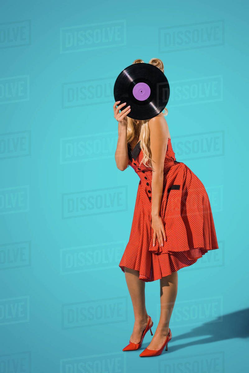 Obscured view of woman in vintage dress covering head with vinyl record on blue background - Royalty-free Stock Photo | Dissolve Obscured view of woman in vintage dress covering head with vinyl record on blue background - Royalty-free Stock Photo | Dissolve