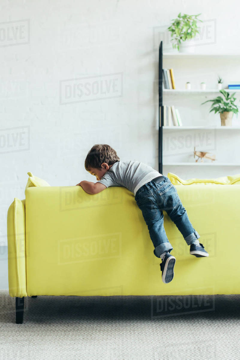 Little Boy Climbing Up On Yellow Sofa At Home Stock Photo Dissolve
