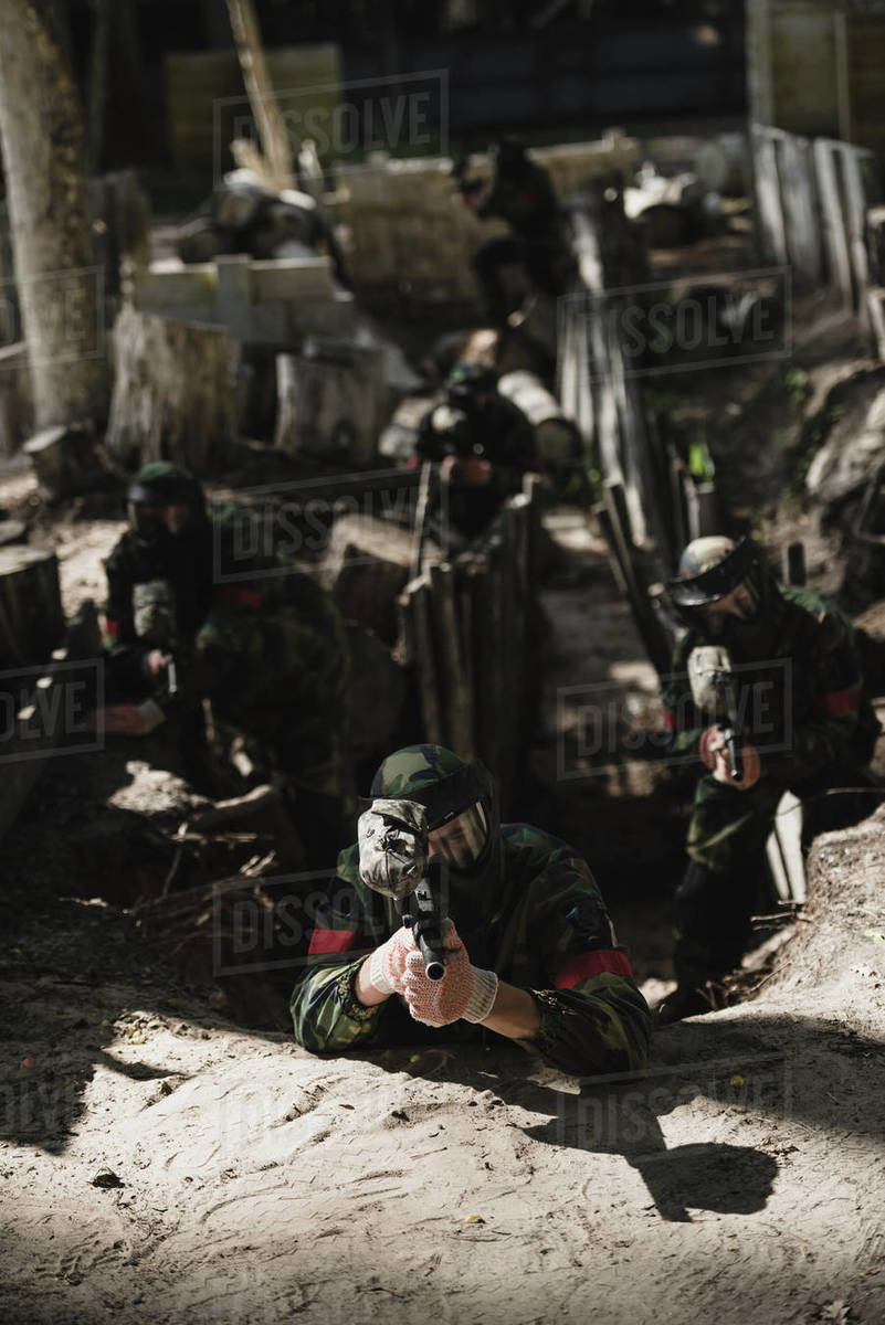 Paintball team in camouflage and protective masks aiming by marker guns