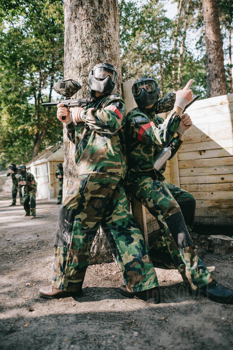 Male paintball player in goggle mask and camouflage holding marker gun