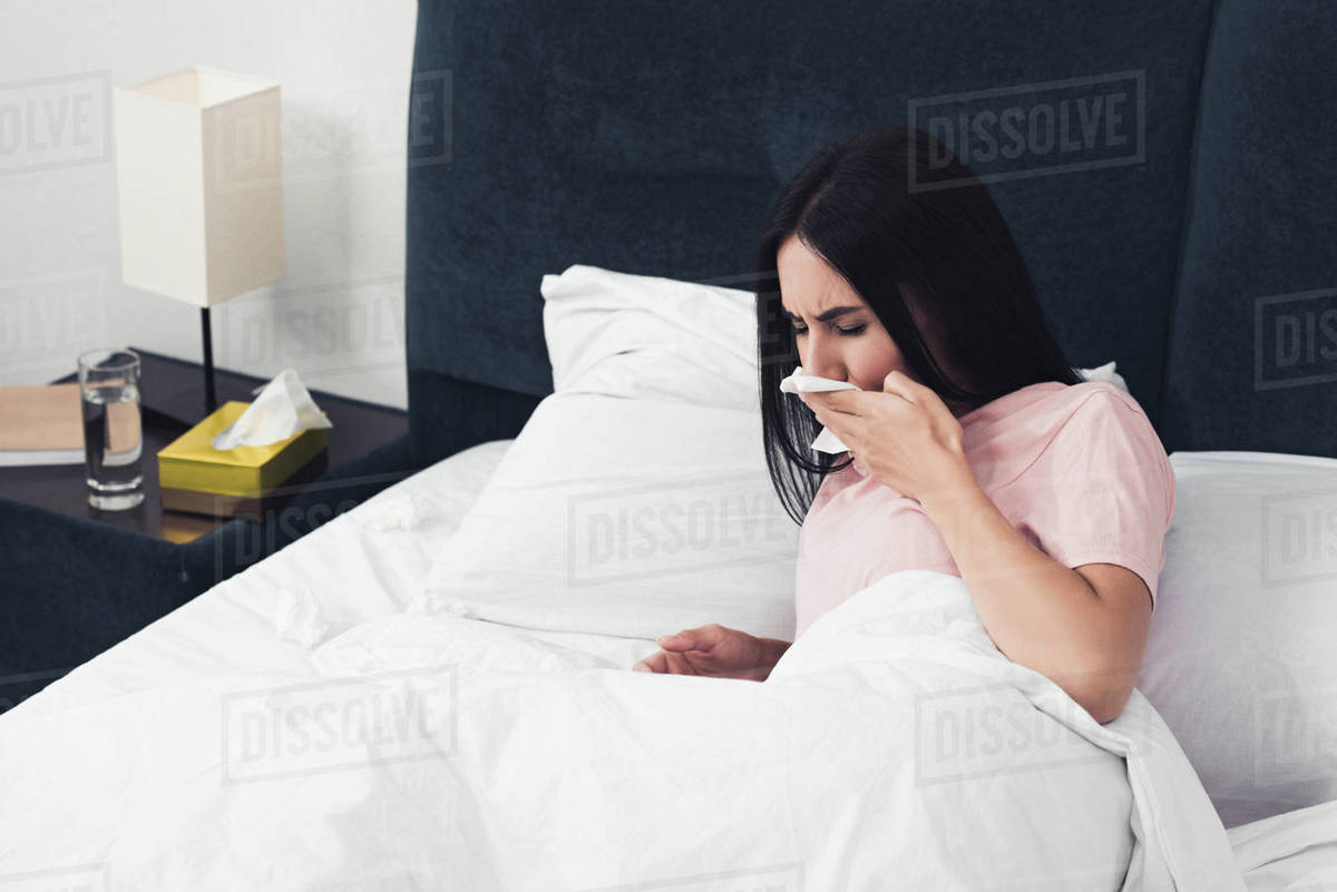 Sick young woman with cough lying in bed with napkins Stock Photo
