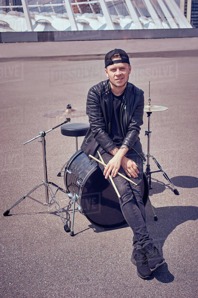 Drummer in black clothing with drum sticks sitting on drum kit on