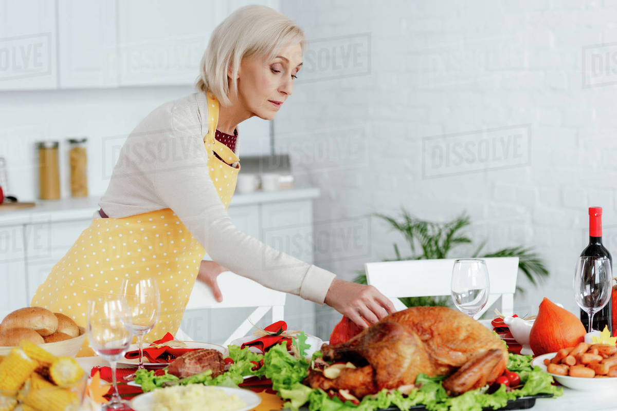 Beautiful senior woman serving table for thanksgiving dinner in kitchen at home Stock Photo