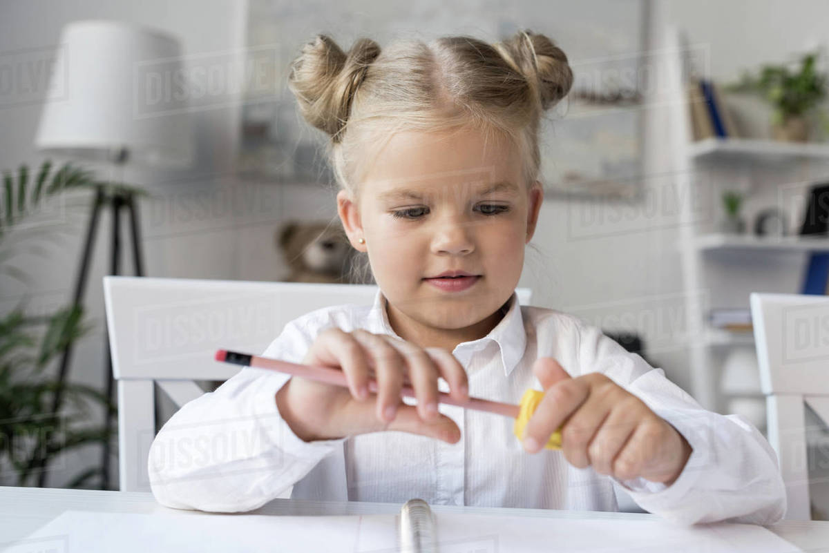 Cute little girl sharpening pencil while preparing for school Stock