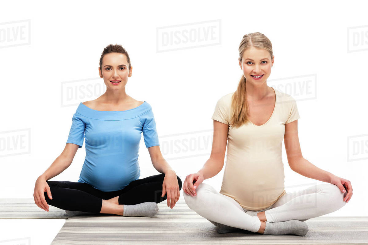 Two beautiful pregnant women sitting on floor and holding hands on
