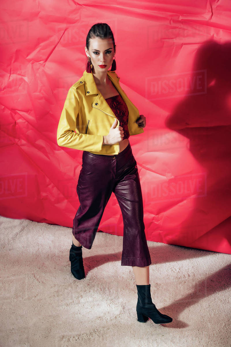 Stylish model posing in yellow leather jacket on red background for