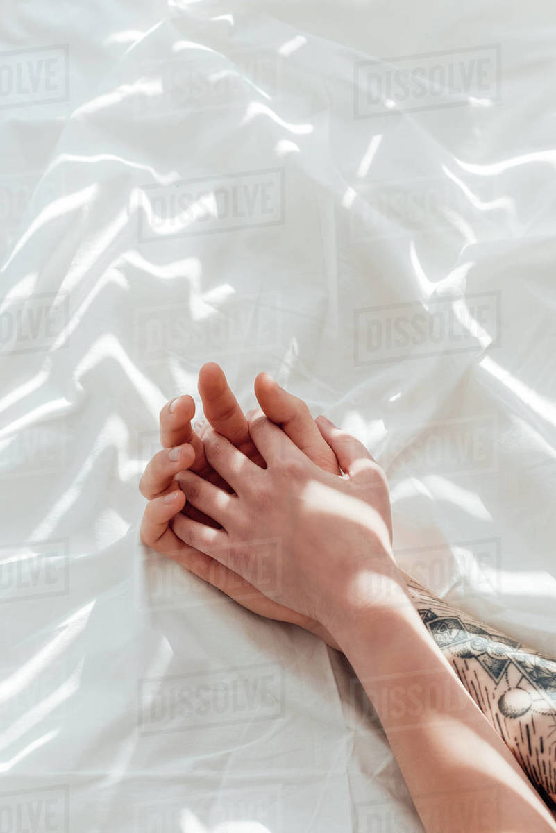 Partial View Of Loving Couple Holding Hands While Lying On White Bed Sheet Stock Photo Dissolve partial view of loving couple holding hands while lying on d2115 176 392