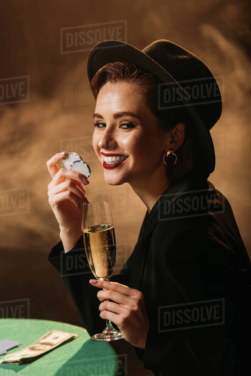 Happy attractive girl in jacket and hat holding glass of champagne and
