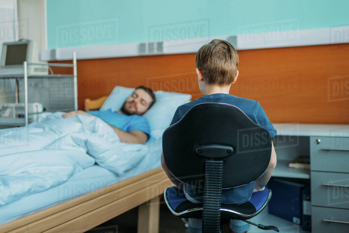 Little son sitting on chair near his sick father sleeping on