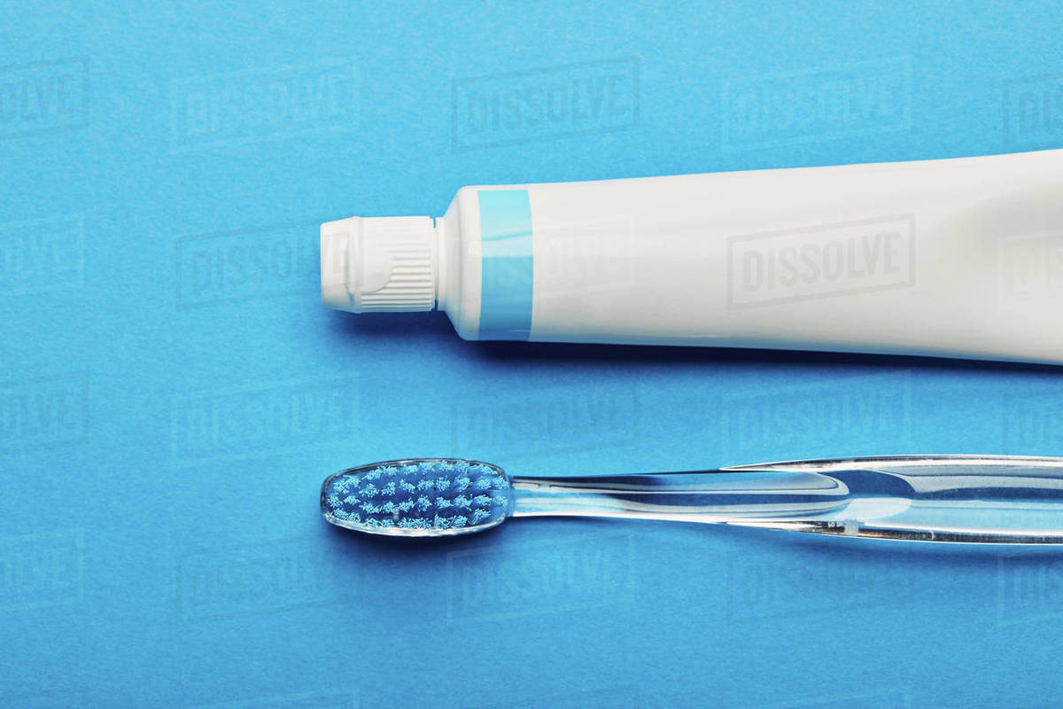 Top view of toothbrush and toothpaste arranged on blue backdrop