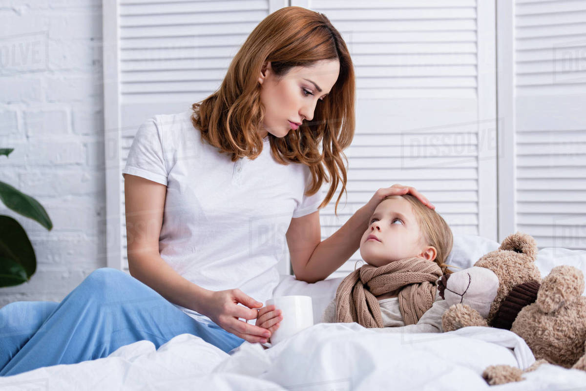 Mother taking care of sick daughter in bedroom and giving her cup of