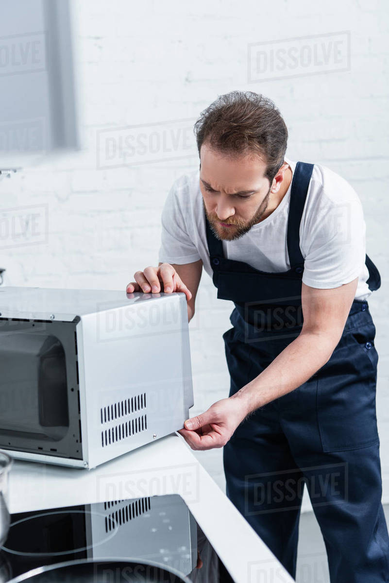 serious adult handyman repairing microwave oven in kitchen Stock