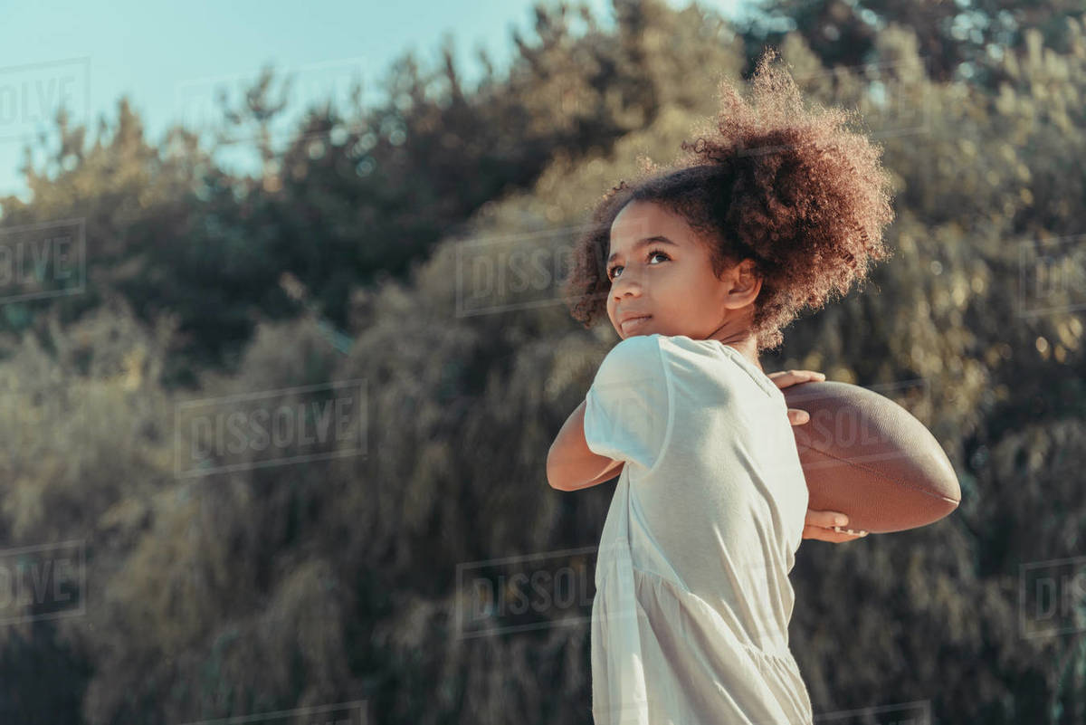 Beautiful African American girl throwing rugby ball and looking away