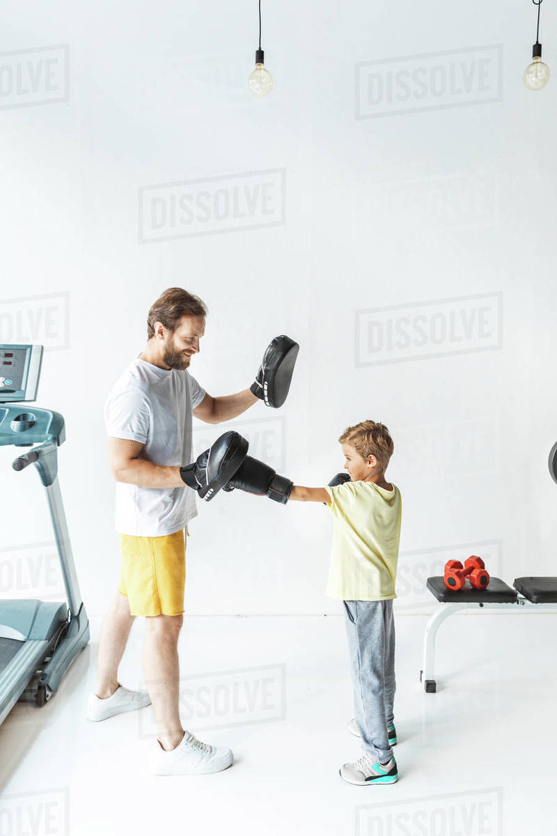 Side view of father and son boxing together in gym Stock Photo Dissolve
