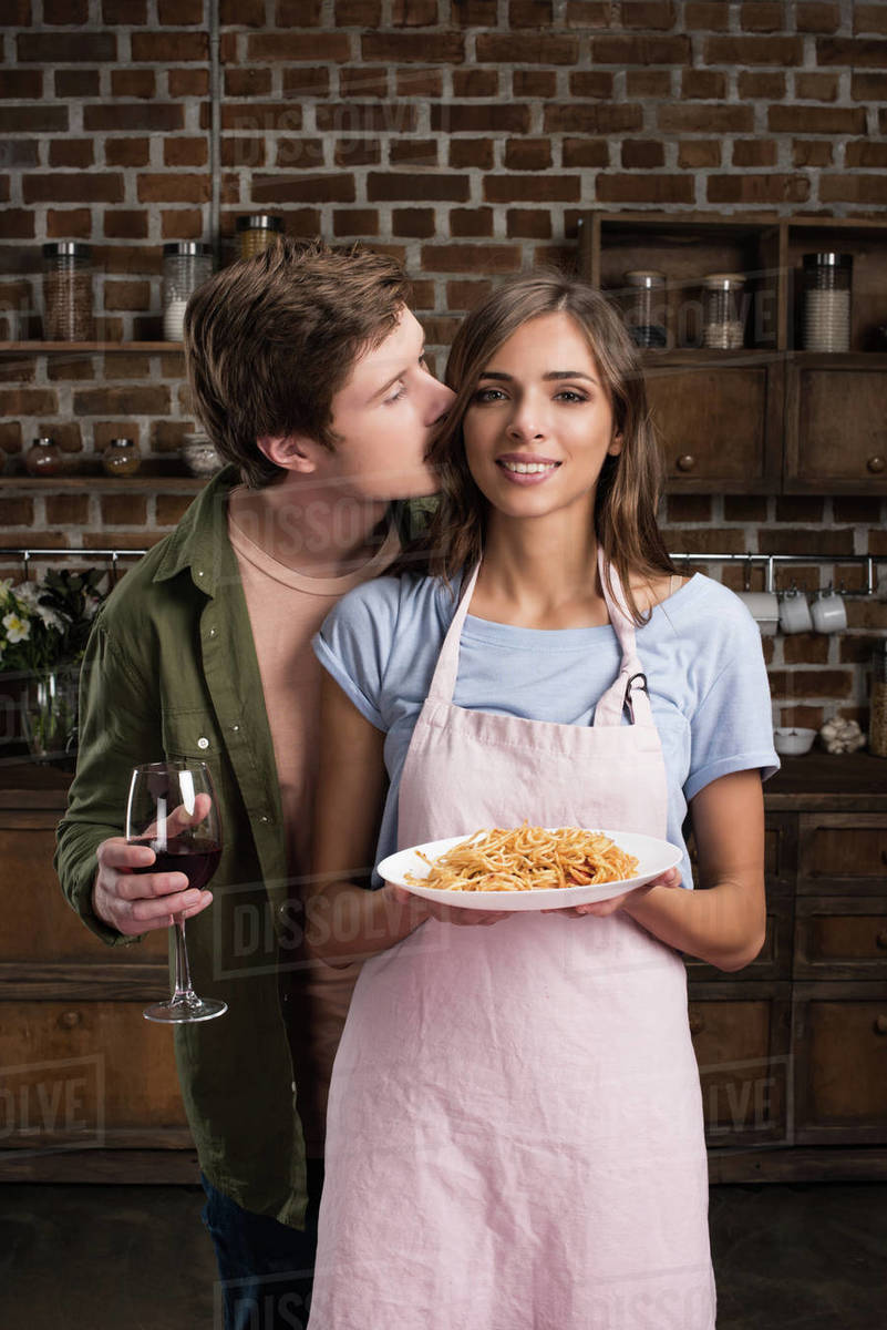 Portrait of man with glass of wine kissing smiling girlfriend with