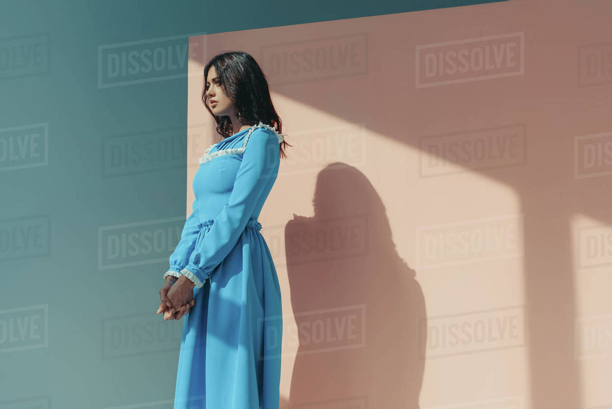 Side view of attractive woman standing in fashionable turquoise dress with  long sleeves and looking away - Royalty-free Stock Photo | Dissolve