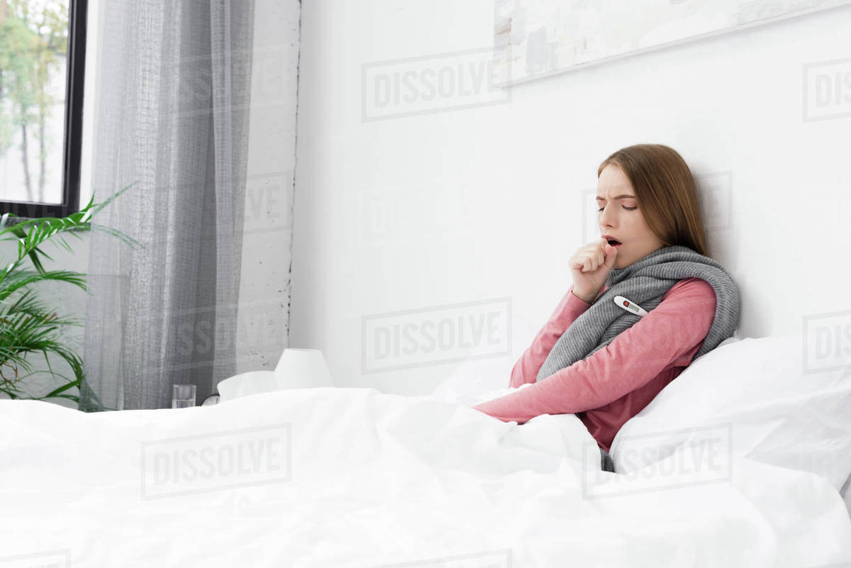 Sick girl with cough lying with thermometer in bed at home Stock