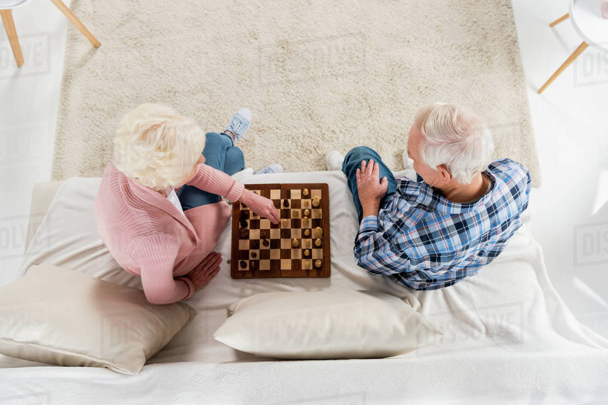 Top View Of Senior Couple Playing Chess At Home On Couch Stock