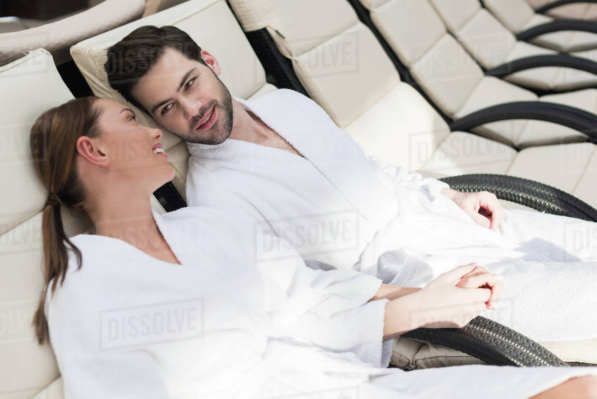 Young couple in bathrobes smiling each other while resting together in