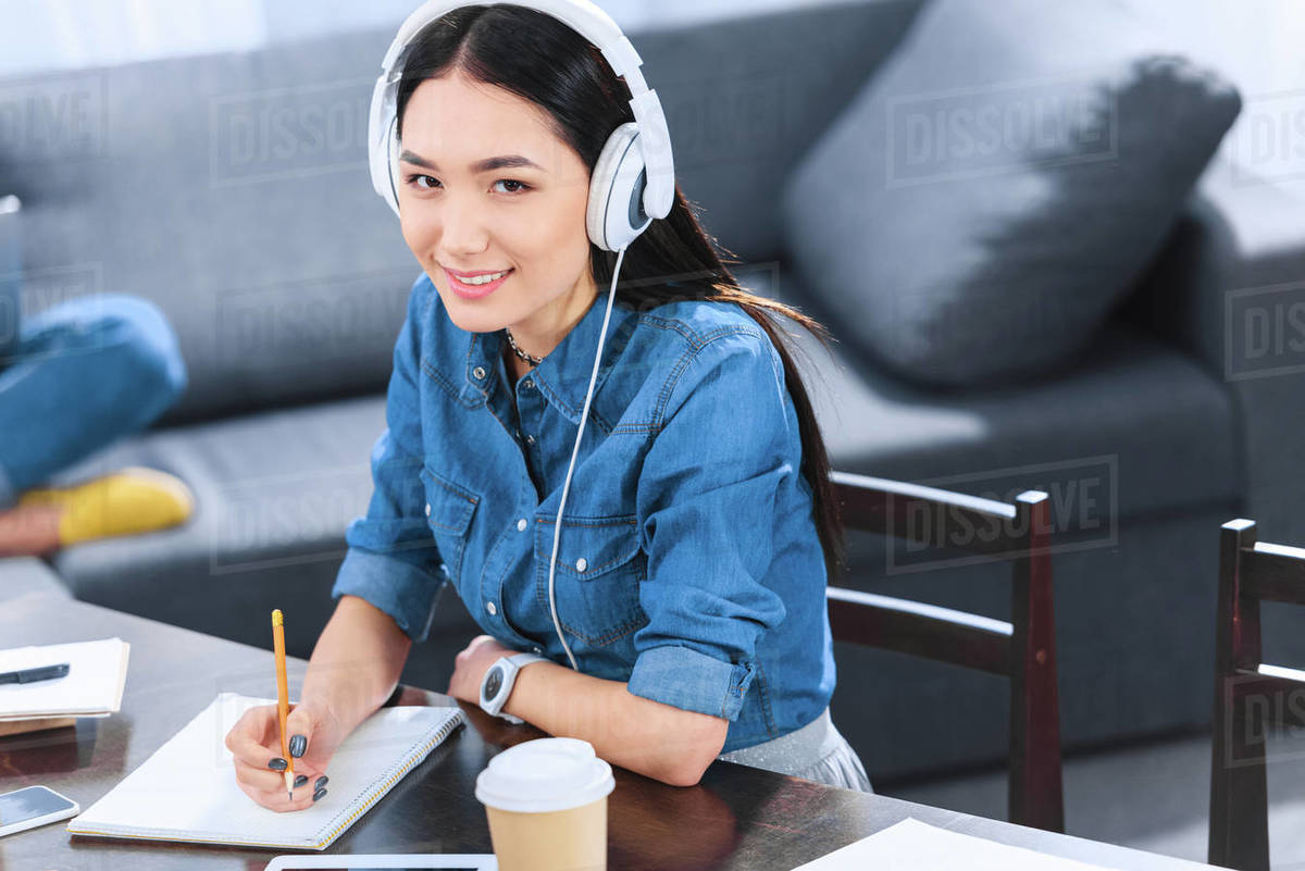Portrait of smiling Asian student in headphones looking at camera ...