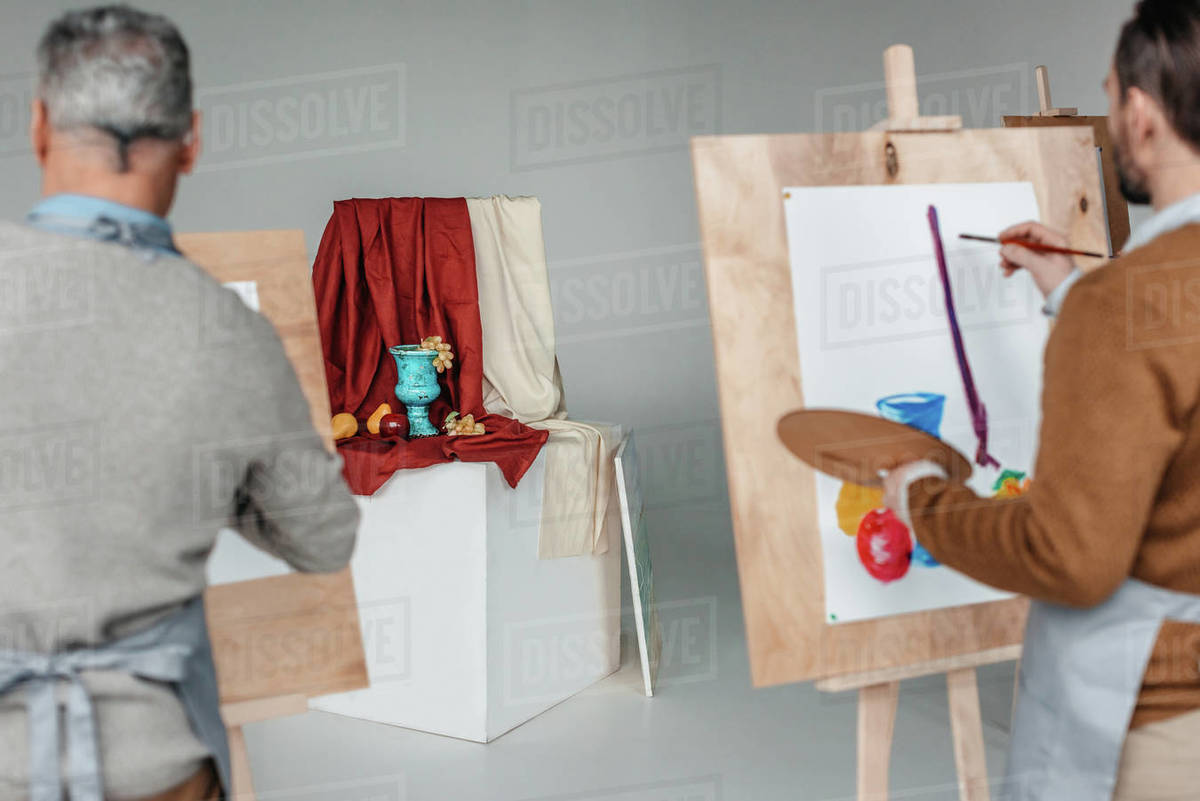 back view of two men painting still life on easels at art class Stock