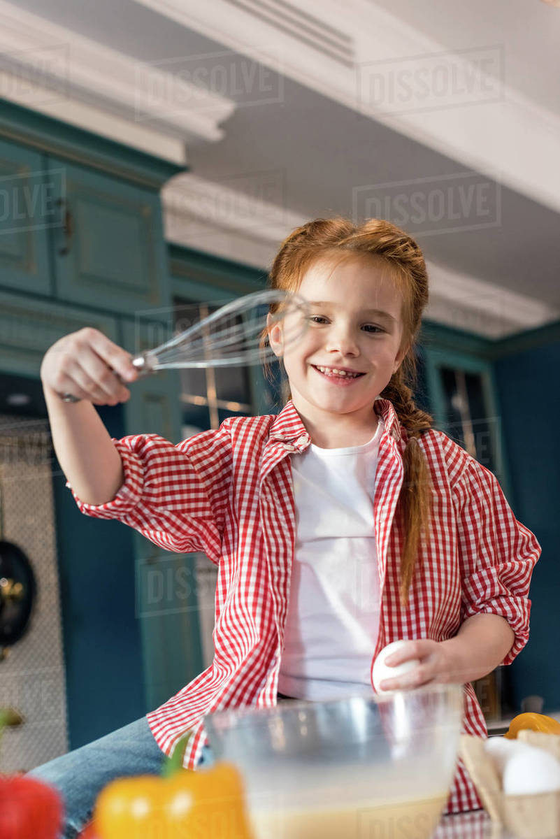 Cute smiling child holding whisk while cooking in kitchen Stock Photo