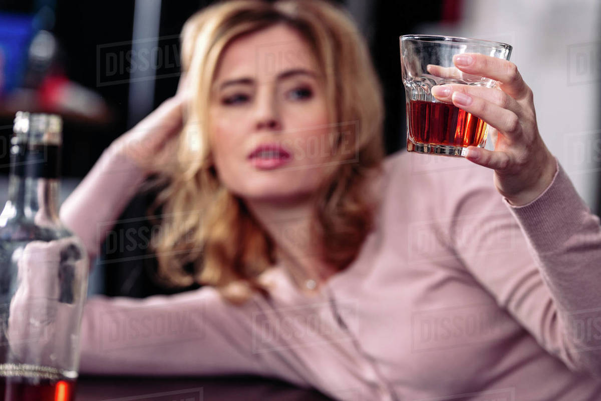 Selective focus of woman looking at glass of alcohol in hand Stock