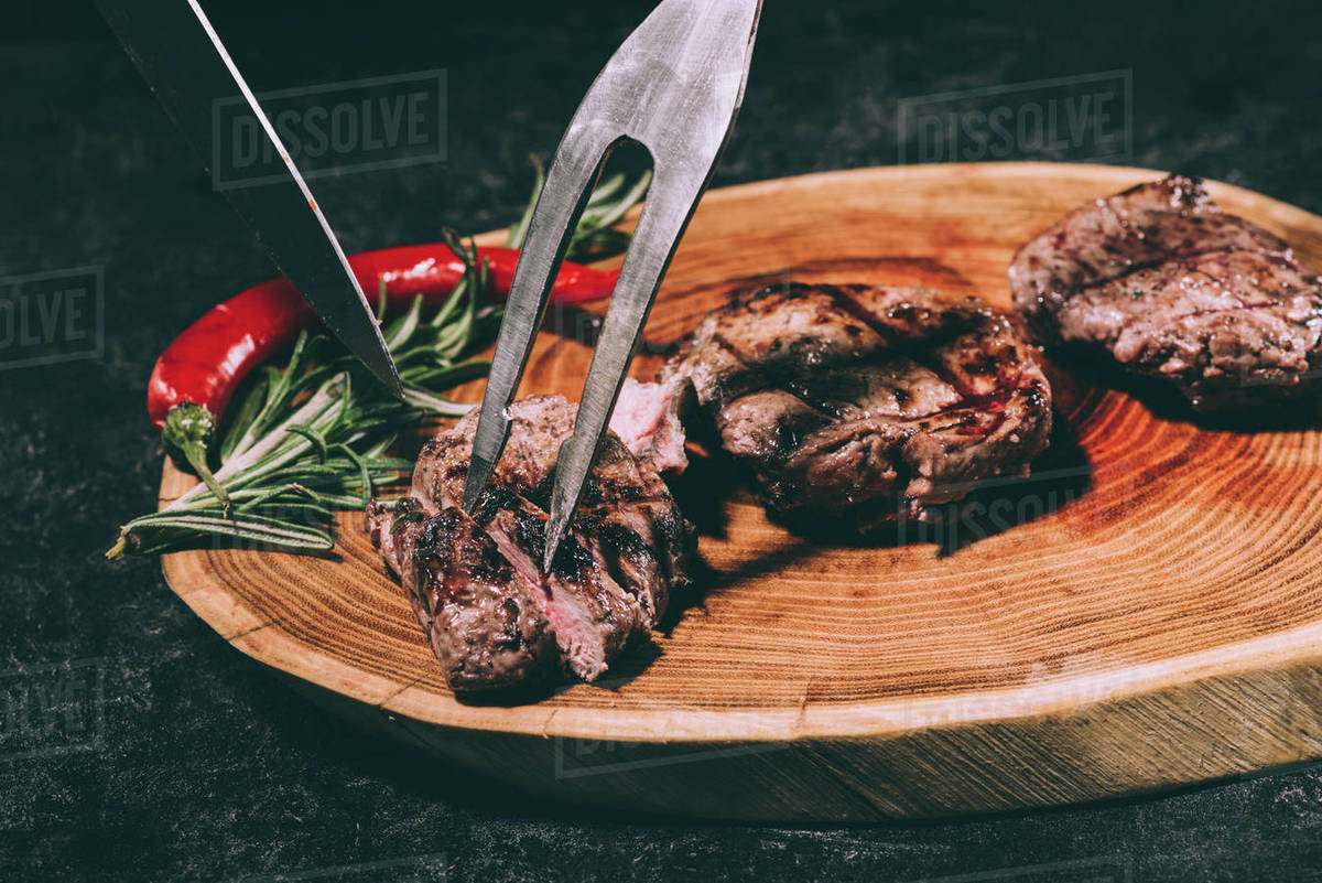 closeup view of meat fork and knife, delicious grilled steaks with