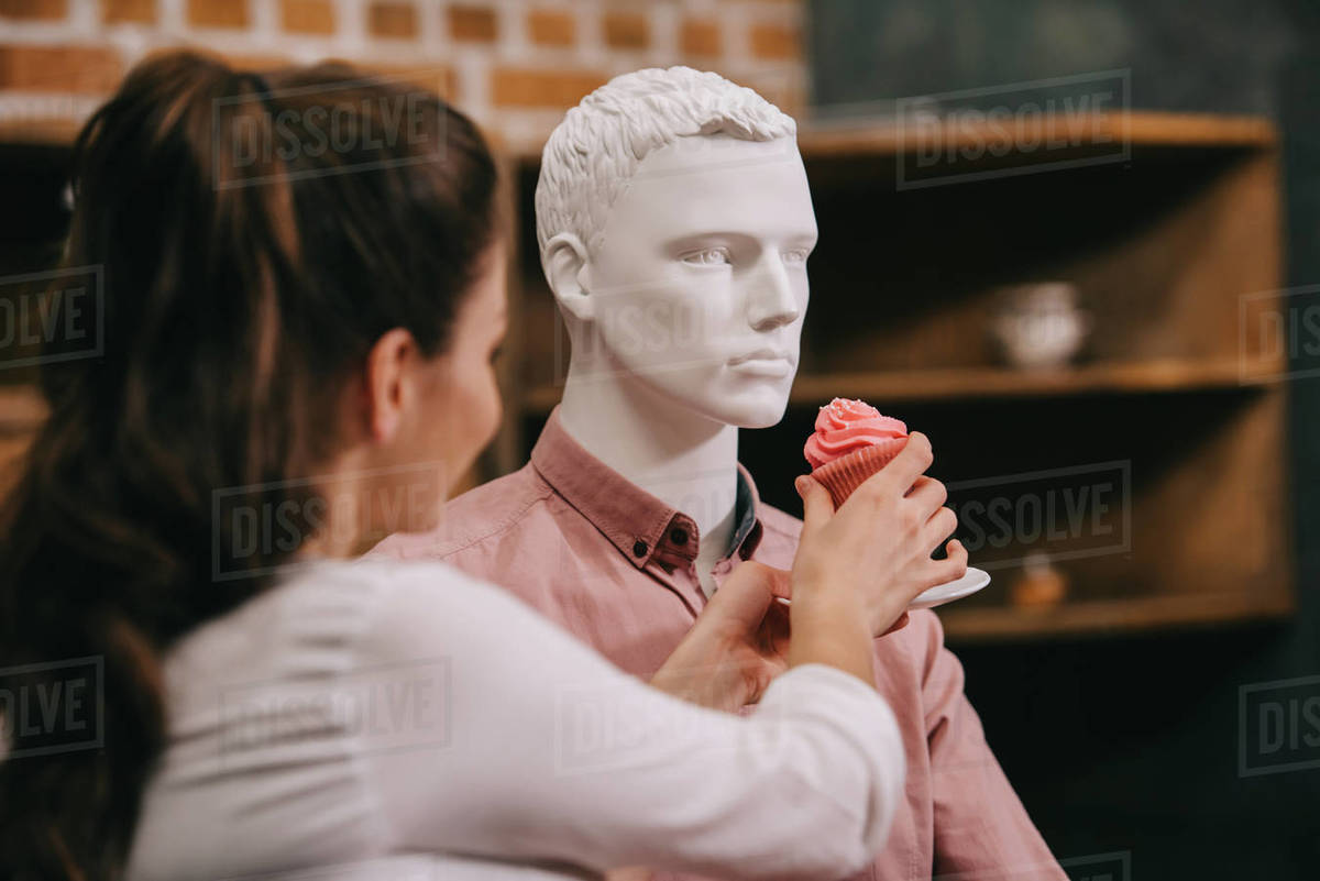 Woman pretending to feed mannequin with cupcake at home, perfect