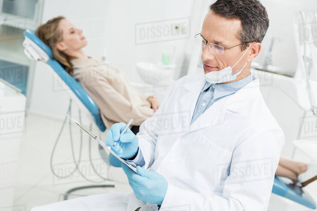 Dentist recording diagnosis while female patient waiting in modern