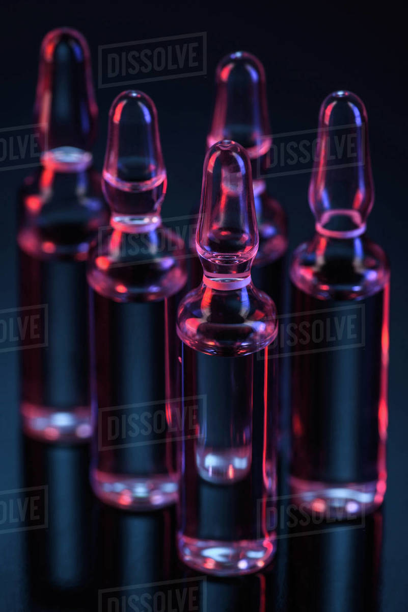 Close up of five transparent glass ampoules with liquid on table on