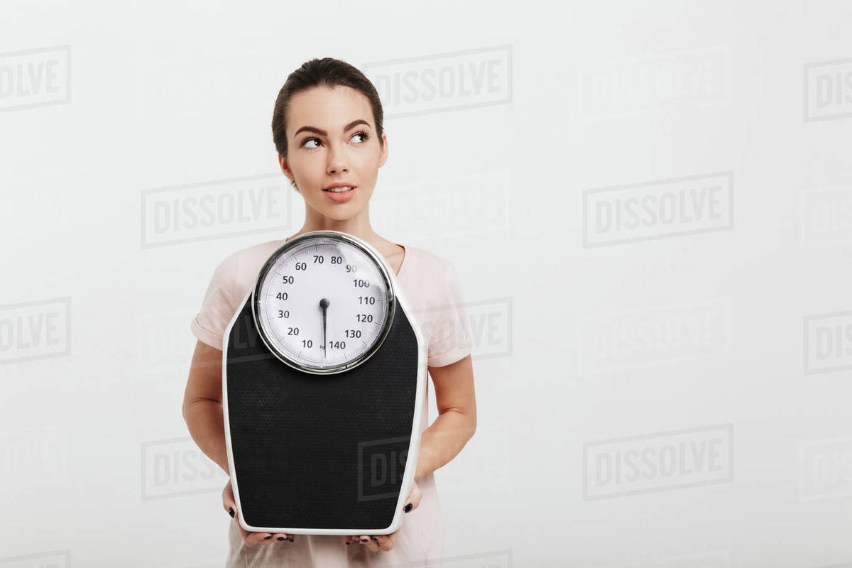 Beautiful girl holding scales and looking away isolated on white ...