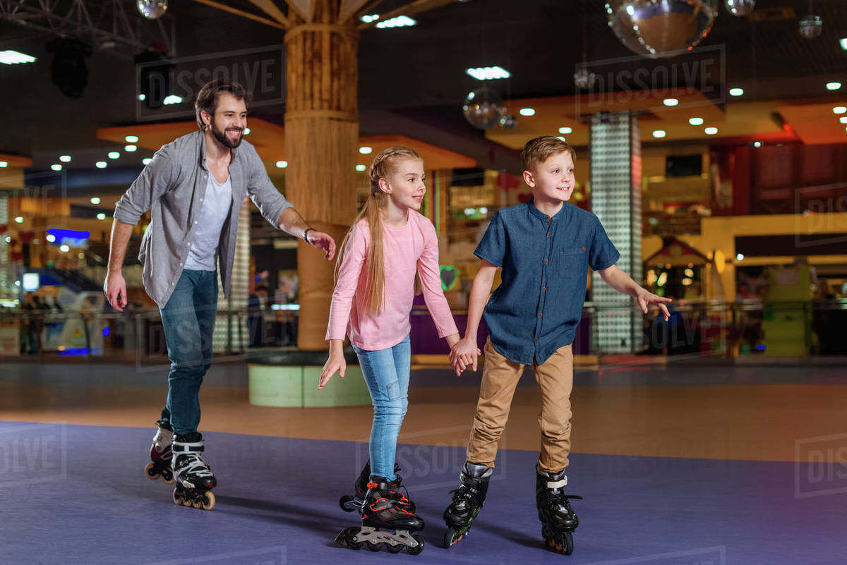Father and little children skating together on roller rink Stock