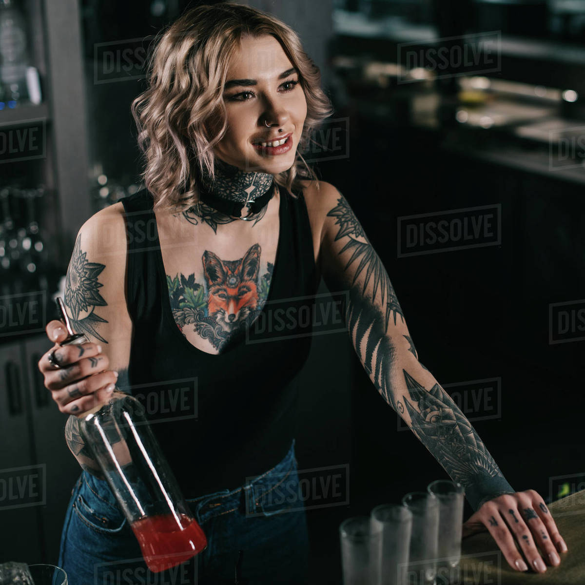 Tattooed bartender holding bottle of alcohol and looking away Stock