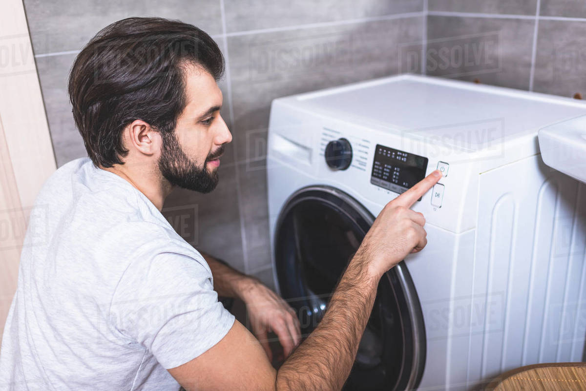Handsome loner setting washing machine program in bathroom Stock