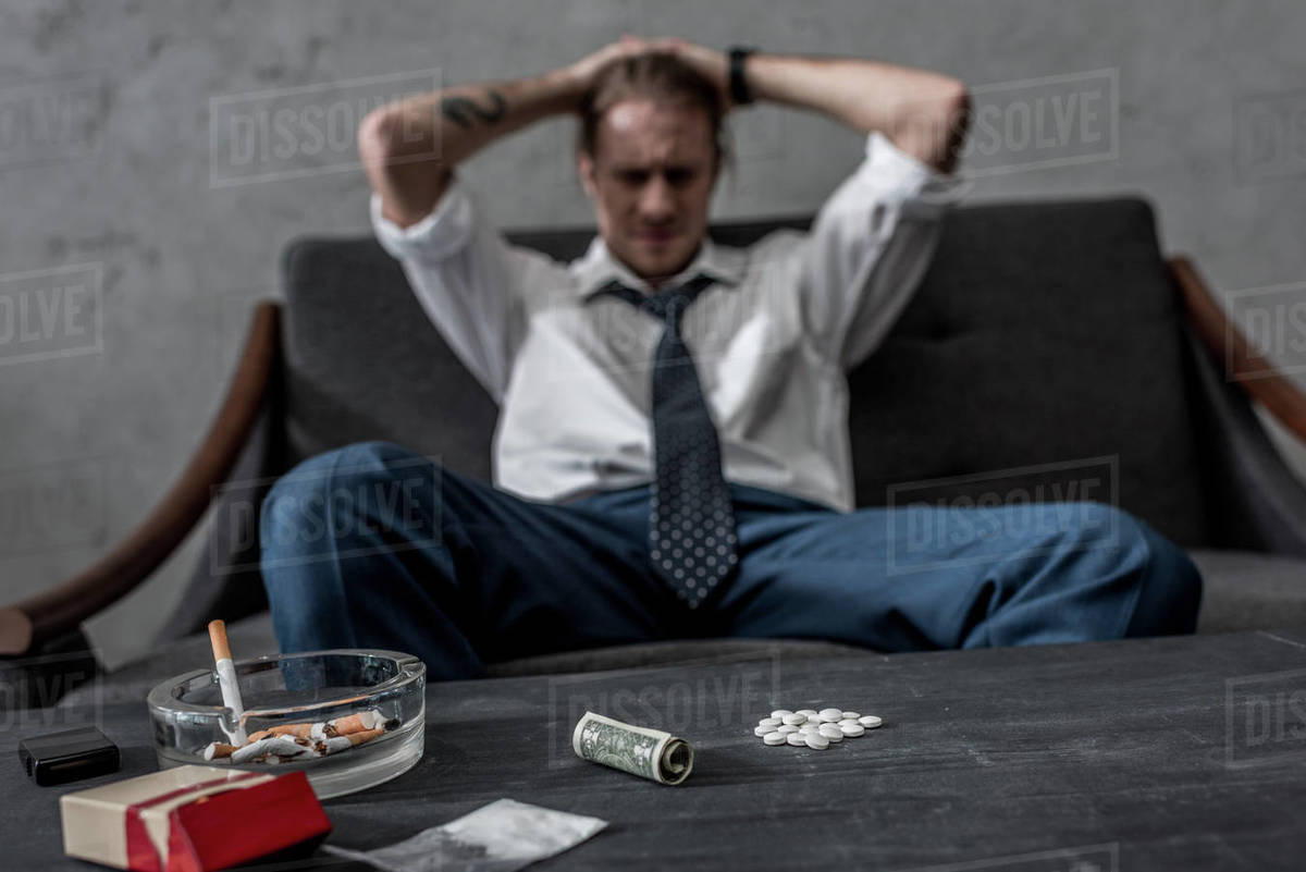 Depressed businessman with drug addiction sitting on couch in front of