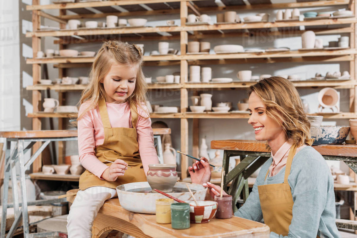 Female teacher and child painting ceramic pot in pottery with