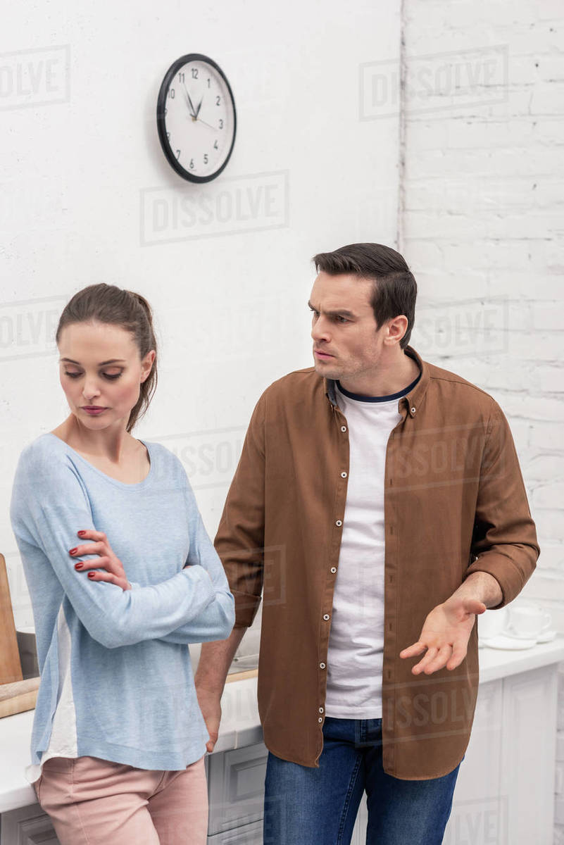 Angry adult man looking at wife while she ignoring him after quarrel at